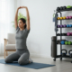 A woman is depicted mid-workout next to a fully stocked mobile fitness equipment storage rack.